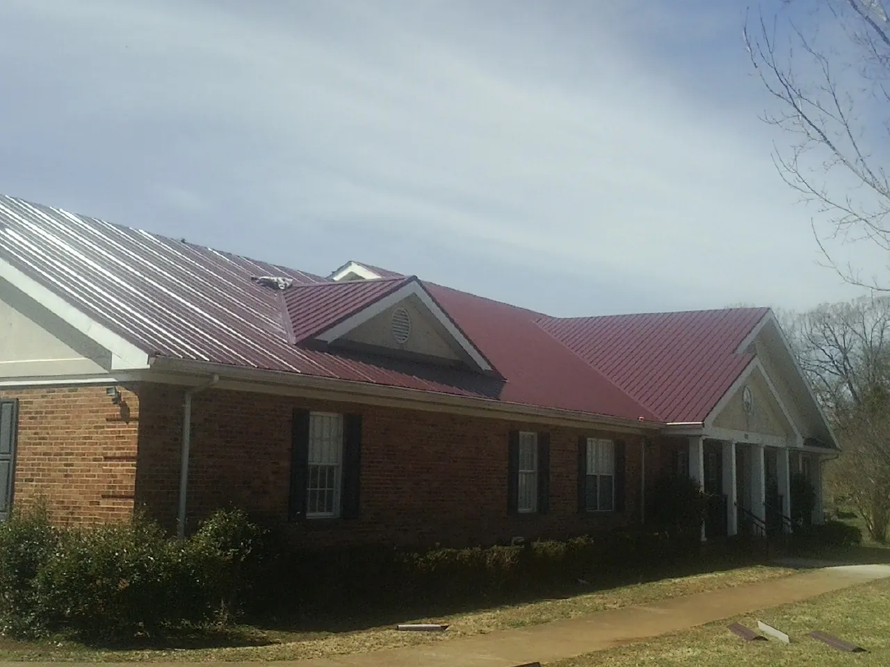 Red metal roof with gabled entries on a long brick building, from a Hail Damage Roof Repair job in Potlatch
