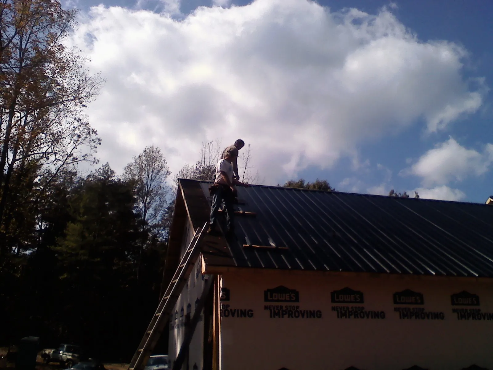 Roofer fastening dark metal panels high against a cloudy sky, from a Roof Inspection job in Potlatch